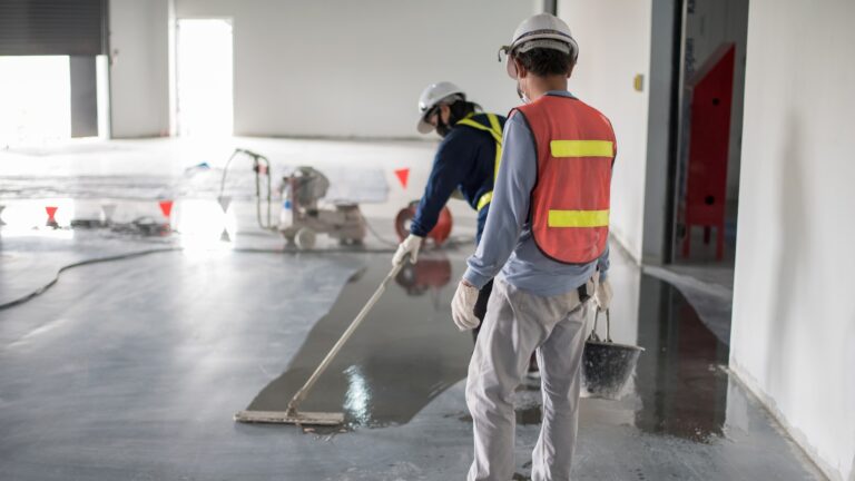 two professional workers applying floor finish on concrete floor in a commercial space with mop.