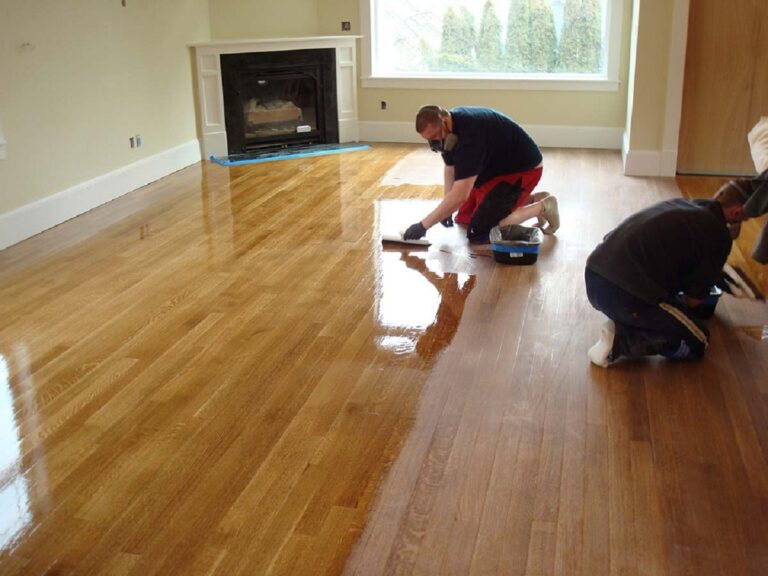 two people applying floor finish on hardwood floor.