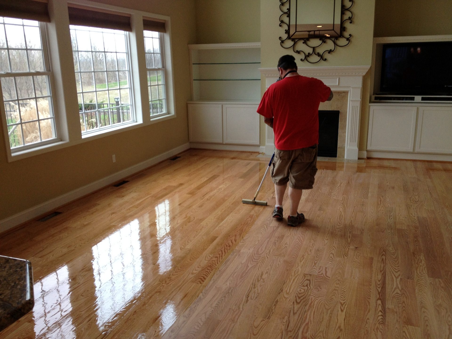 a man applying polyurethane coating on hardwood floor.