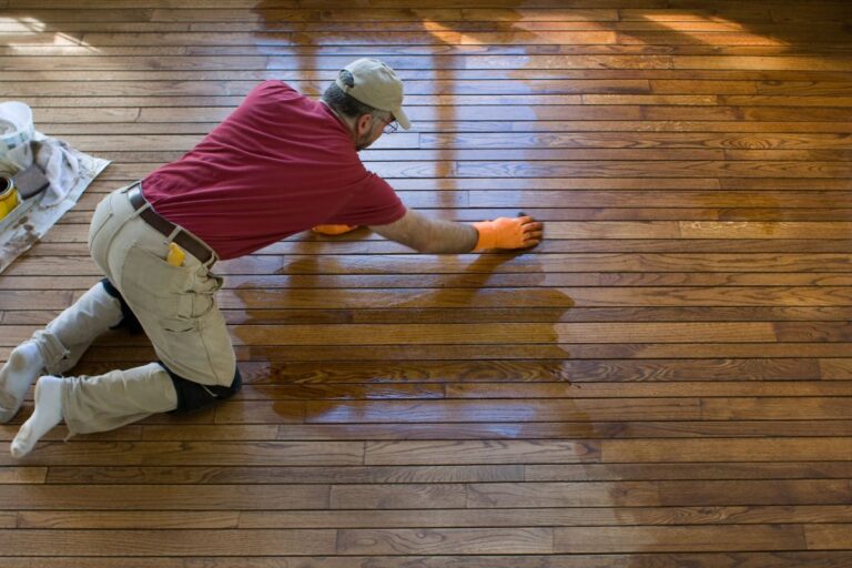 a man on his knees waxing a hardwood floor for shinning.