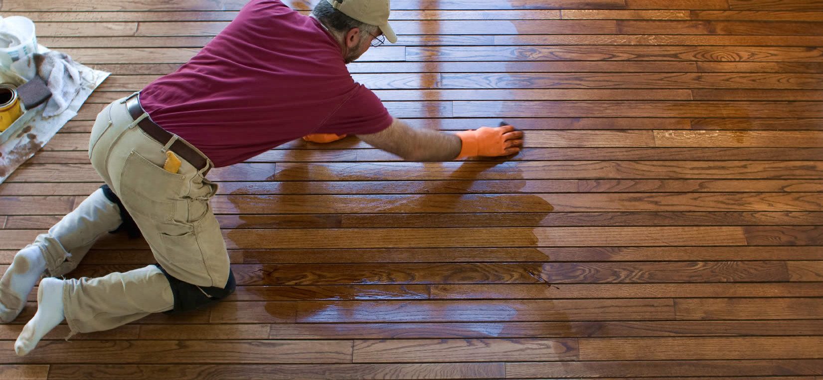 a man on his knees polishing hardwood floor.